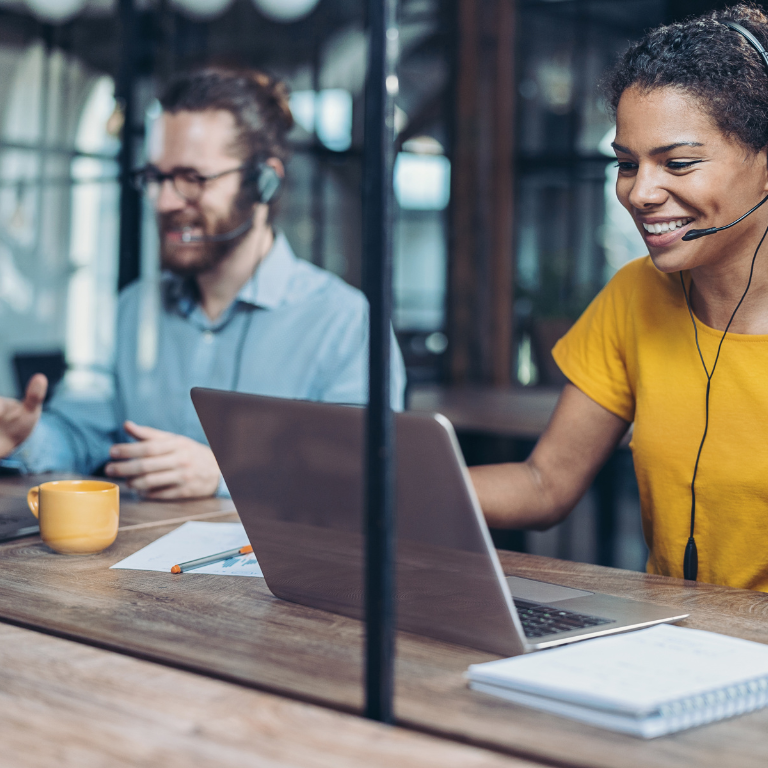 Two individuals at a desk wearing headsets, focused on responding to emails and engaging in communication.